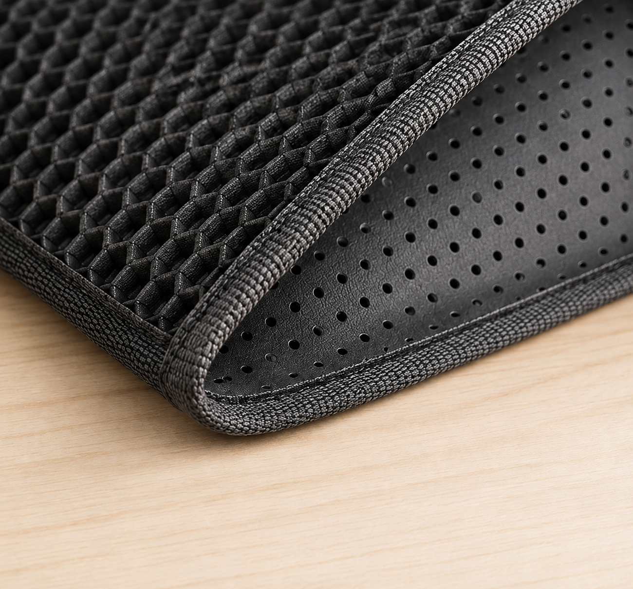 Close-up of a black mesh and perforated pad with a stitched edge, shown on a light wood surface.
